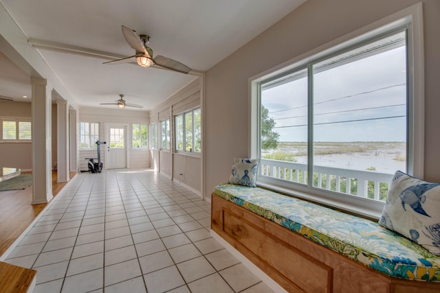 sunroom / solarium with a water view, ceiling fan, a healthy amount of sunlight, and ornate columns