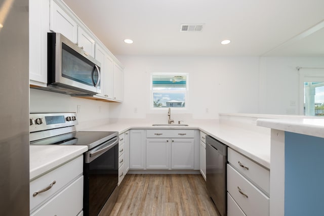 kitchen with stainless steel appliances, white cabinetry, sink, and light hardwood / wood-style floors