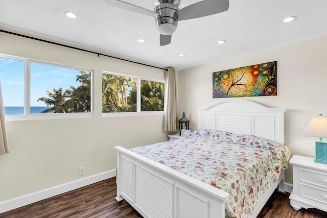 bedroom with dark hardwood / wood-style flooring, a textured ceiling, ceiling fan, and a water view