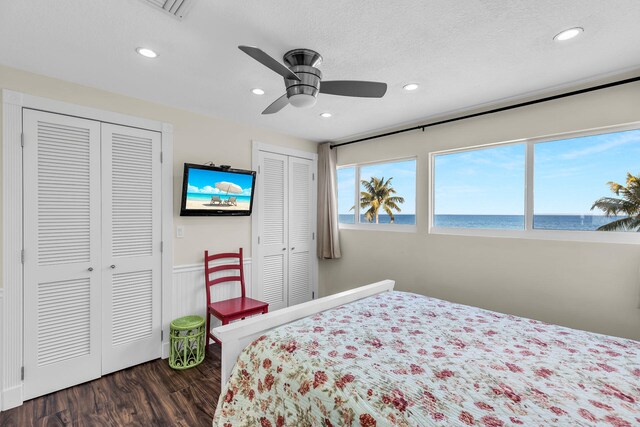 bedroom with ceiling fan, two closets, dark hardwood / wood-style floors, and a textured ceiling