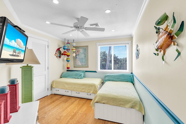 bedroom featuring ceiling fan, light hardwood / wood-style flooring, ornamental molding, and a textured ceiling