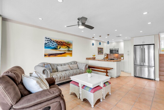 tiled living room featuring ceiling fan, ornamental molding, sink, and a textured ceiling