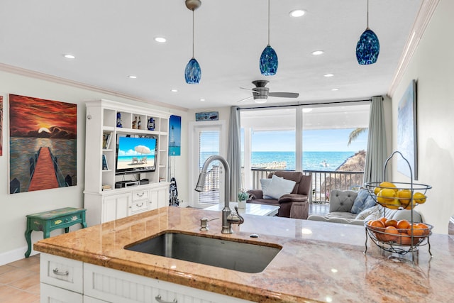 kitchen with pendant lighting, white cabinetry, sink, light stone counters, and crown molding