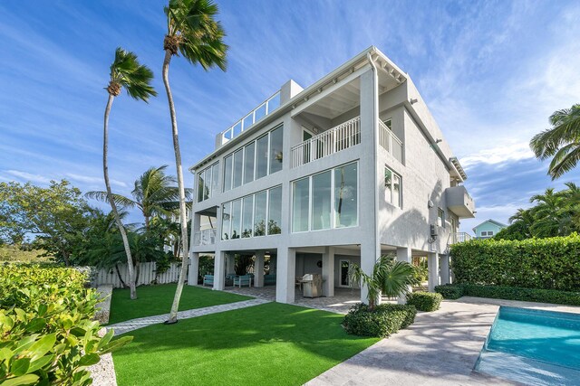 back of house with a balcony, a fenced in pool, a patio area, and a lawn