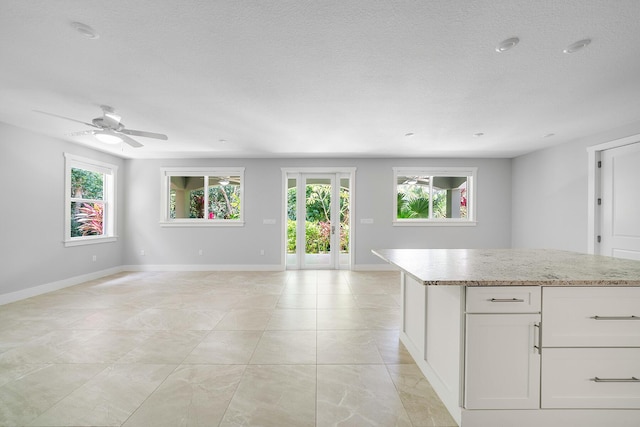 kitchen featuring light stone counters, a textured ceiling, white cabinets, and a kitchen island