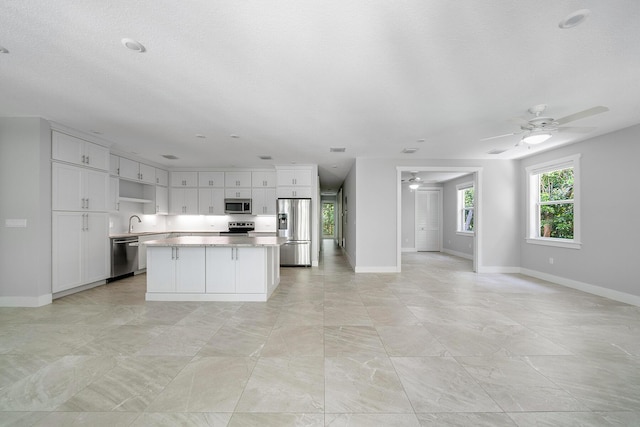 kitchen with a kitchen island, appliances with stainless steel finishes, white cabinets, ceiling fan, and a textured ceiling