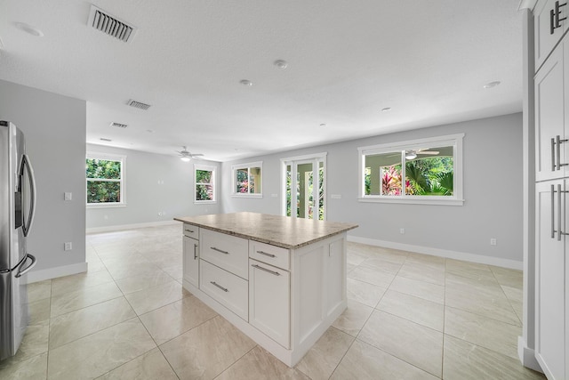 kitchen with light tile patterned floors, ceiling fan, stainless steel refrigerator with ice dispenser, white cabinets, and a kitchen island