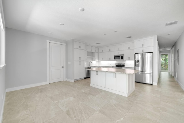 kitchen with sink, appliances with stainless steel finishes, a kitchen island, light stone countertops, and white cabinets