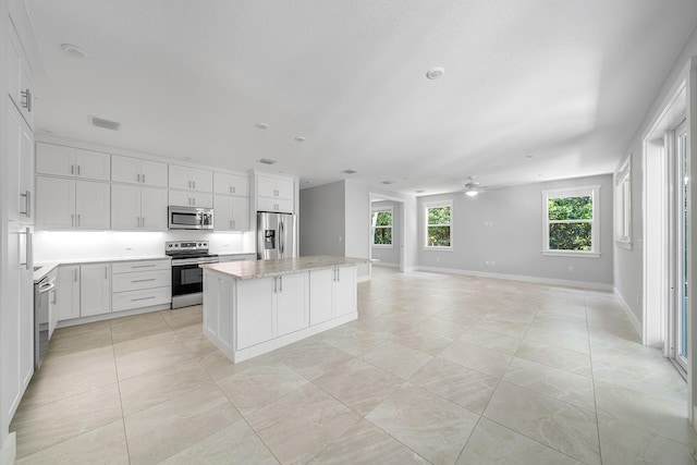 kitchen featuring white cabinetry, a kitchen island, ceiling fan, stainless steel appliances, and light stone countertops