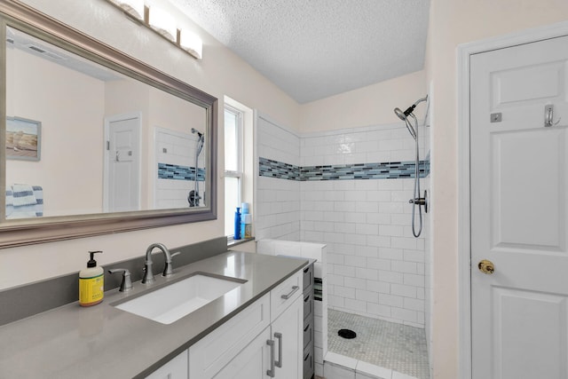 bathroom with a tile shower, vanity, and a textured ceiling