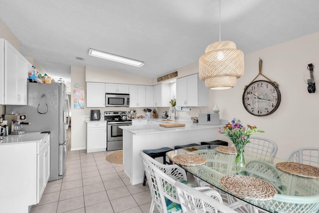 kitchen with light tile patterned flooring, white cabinetry, hanging light fixtures, kitchen peninsula, and stainless steel appliances