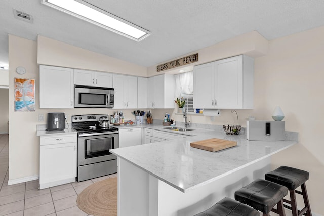 kitchen featuring a breakfast bar area, kitchen peninsula, white cabinets, and appliances with stainless steel finishes