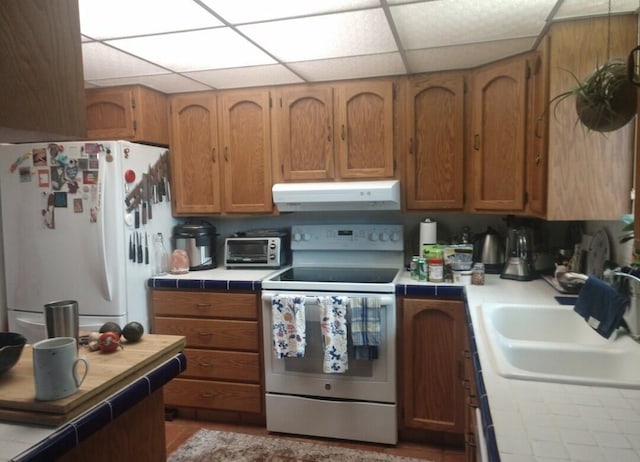 kitchen with white appliances, tile countertops, brown cabinetry, a sink, and under cabinet range hood