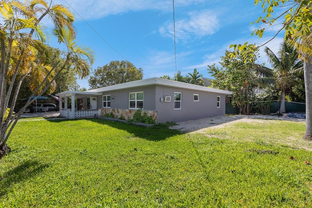 rear view of house with a lawn, fence, and stucco siding