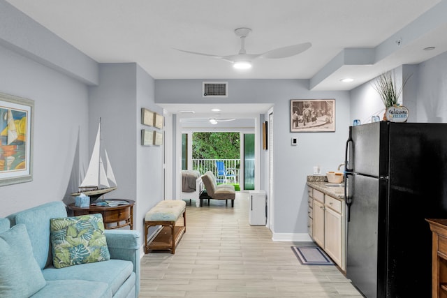 kitchen featuring light stone counters, light wood-type flooring, ceiling fan, and black fridge