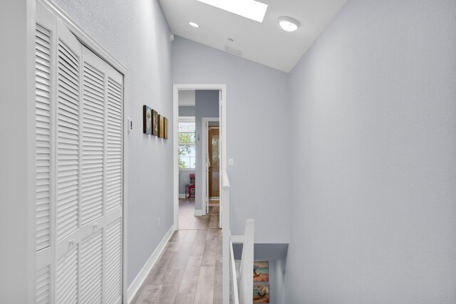 corridor with light hardwood / wood-style floors and vaulted ceiling with skylight