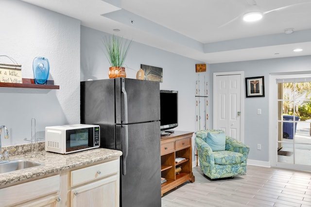 kitchen with black refrigerator, a raised ceiling, sink, and light brown cabinets