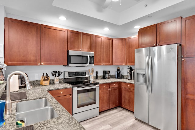 kitchen with sink, ceiling fan, appliances with stainless steel finishes, light stone counters, and light hardwood / wood-style floors