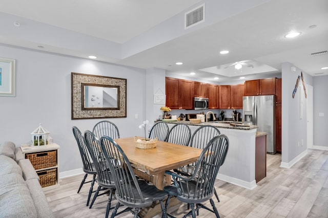 dining space featuring sink, light hardwood / wood-style floors, a raised ceiling, and ceiling fan