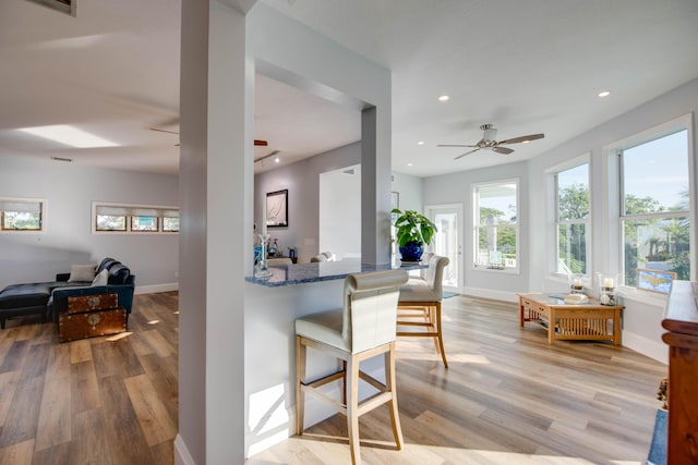 kitchen featuring a breakfast bar, stone countertops, ceiling fan, kitchen peninsula, and light wood-type flooring