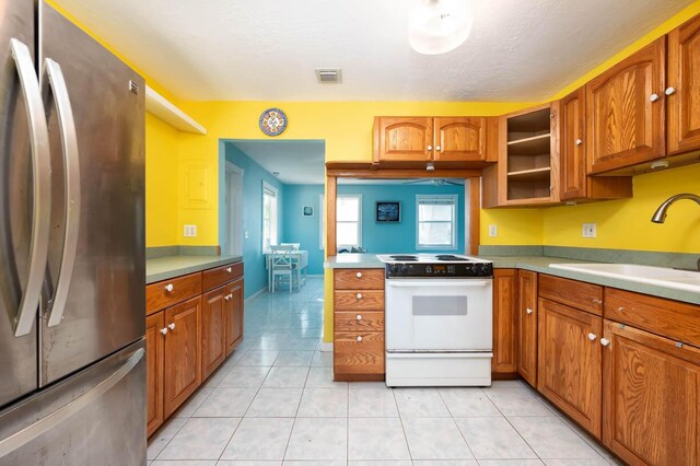 kitchen featuring white electric stove, sink, light tile patterned floors, and stainless steel refrigerator