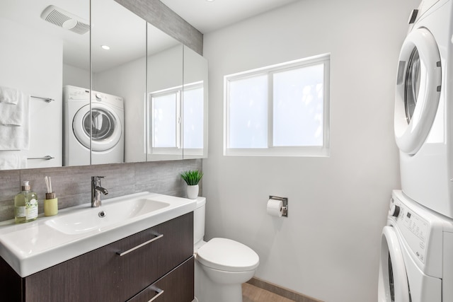 bathroom featuring toilet, stacked washer and dryer, vanity, visible vents, and backsplash