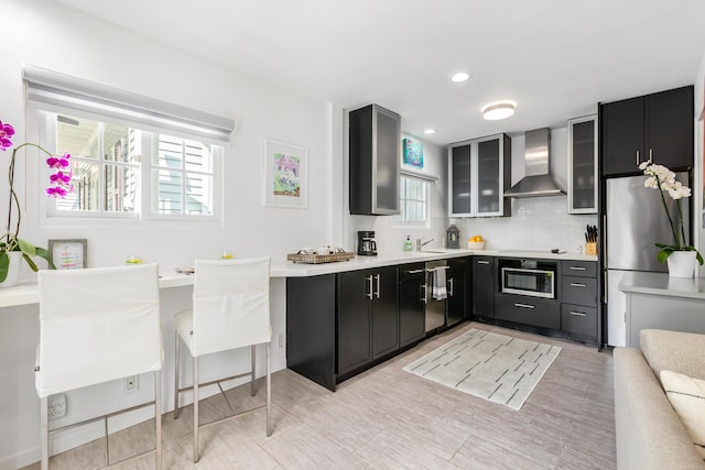 kitchen featuring dark cabinetry, light countertops, glass insert cabinets, oven, and wall chimney exhaust hood