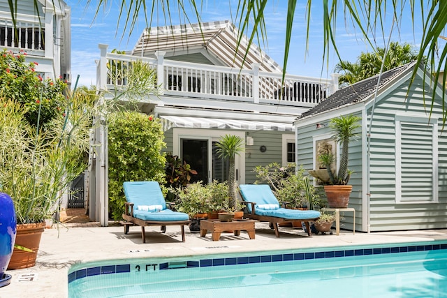 back of house with a balcony, an outdoor pool, an outdoor structure, and a patio