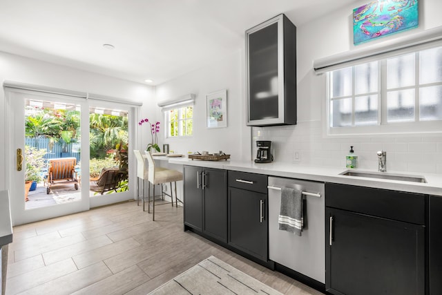 kitchen featuring light countertops, stainless steel dishwasher, a sink, and glass insert cabinets