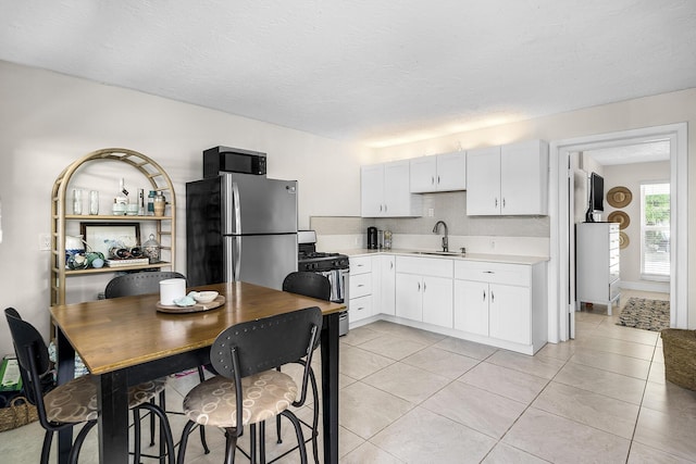 kitchen with sink, tasteful backsplash, light tile patterned floors, stainless steel appliances, and white cabinets