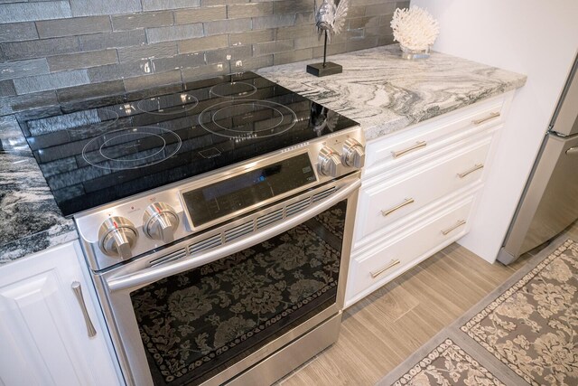 kitchen featuring white cabinetry, stainless steel appliances, tasteful backsplash, light stone countertops, and light hardwood / wood-style floors