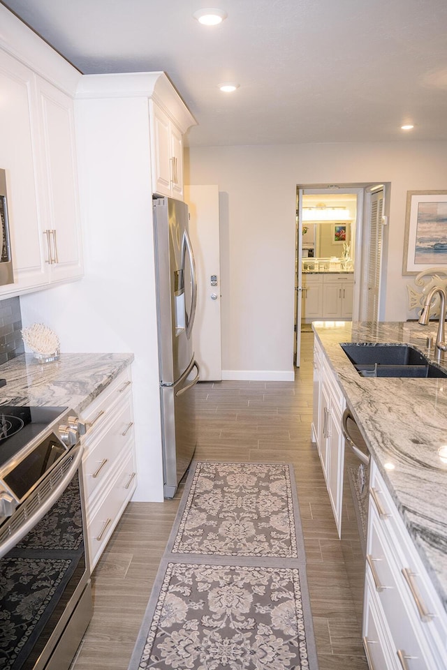 kitchen with white cabinetry, stainless steel appliances, sink, and light stone counters