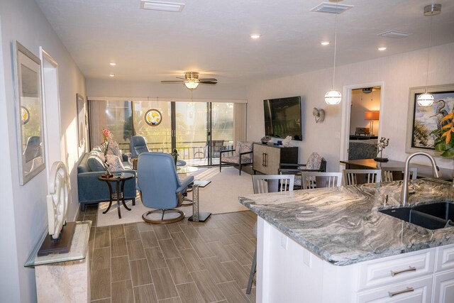 kitchen featuring white cabinetry, sink, hanging light fixtures, ceiling fan, and light stone counters