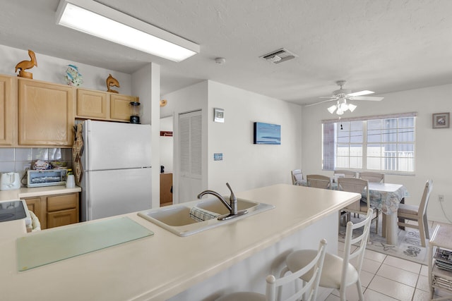 kitchen featuring light brown cabinetry, sink, light tile patterned floors, a kitchen breakfast bar, and white fridge