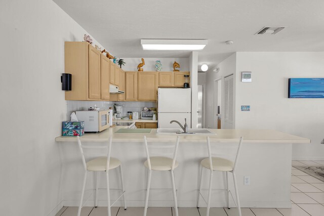 kitchen with a breakfast bar, sink, kitchen peninsula, light brown cabinets, and white appliances