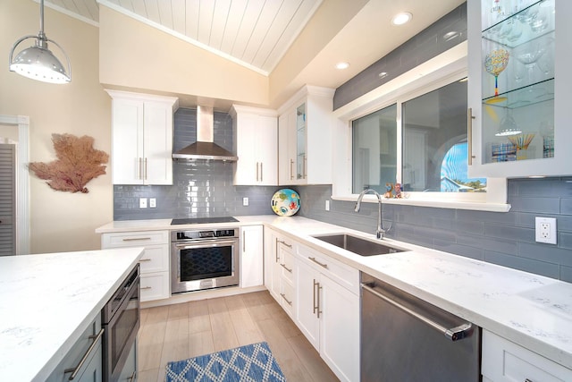 kitchen featuring pendant lighting, wall chimney range hood, white cabinets, and appliances with stainless steel finishes