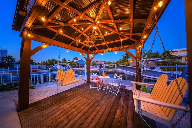 deck at dusk with a gazebo, a water view, and a dock