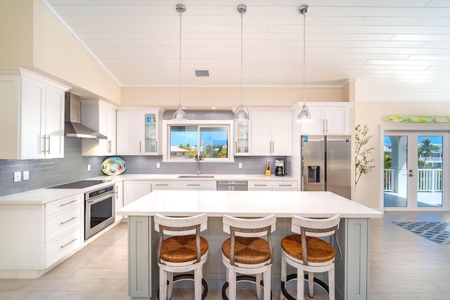 kitchen featuring wall chimney exhaust hood, stainless steel appliances, hanging light fixtures, and a kitchen island