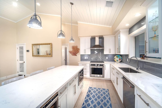 kitchen with sink, white cabinetry, pendant lighting, stainless steel appliances, and wall chimney range hood