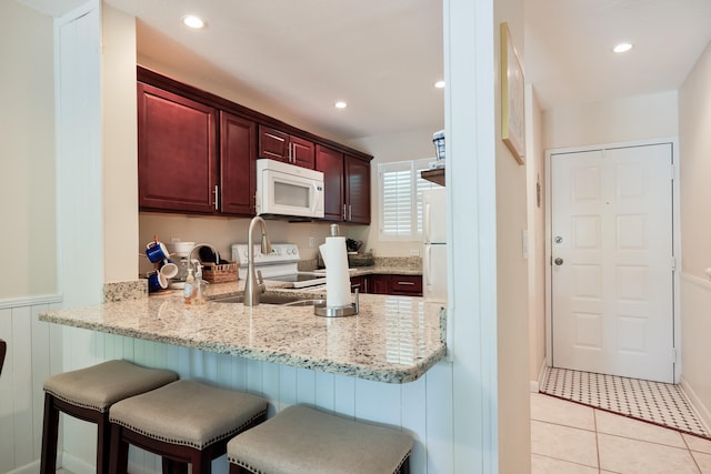 kitchen with light stone counters, white appliances, kitchen peninsula, and light tile patterned flooring