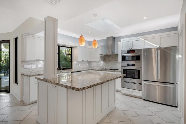 kitchen with a warming drawer, stainless steel appliances, wall chimney exhaust hood, and a wealth of natural light