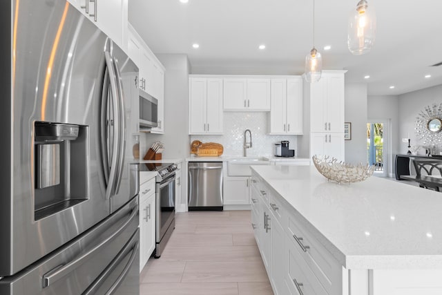 kitchen featuring sink, white cabinetry, a center island, hanging light fixtures, and stainless steel appliances