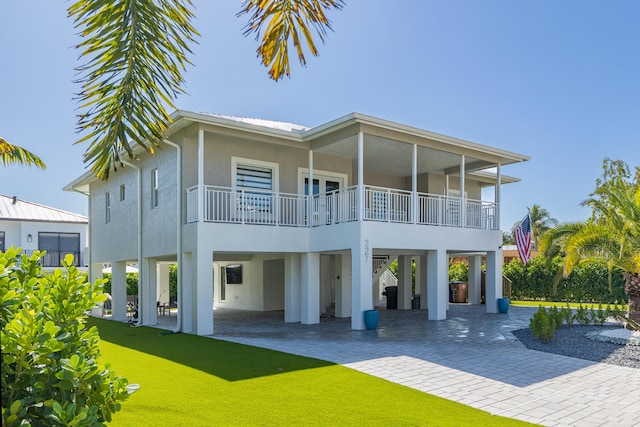 back of property featuring a carport, a balcony, and a lawn