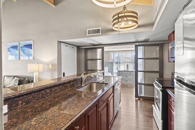 kitchen with sink, dark hardwood / wood-style floors, dark stone counters, and appliances with stainless steel finishes