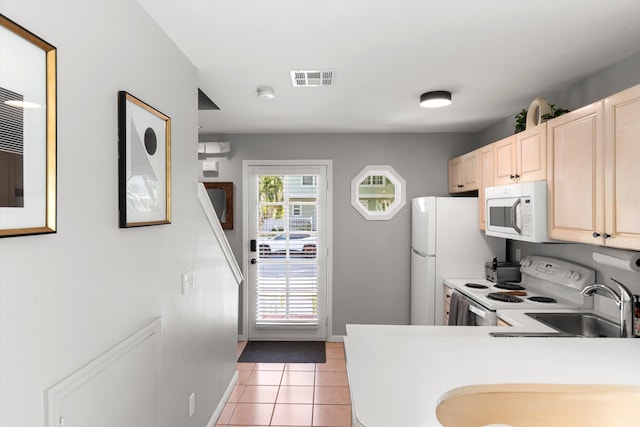 kitchen with white appliances, light tile patterned floors, visible vents, light brown cabinetry, and a sink