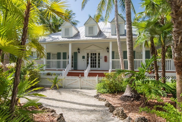 cape cod house featuring driveway, a fenced front yard, metal roof, a gate, and a porch