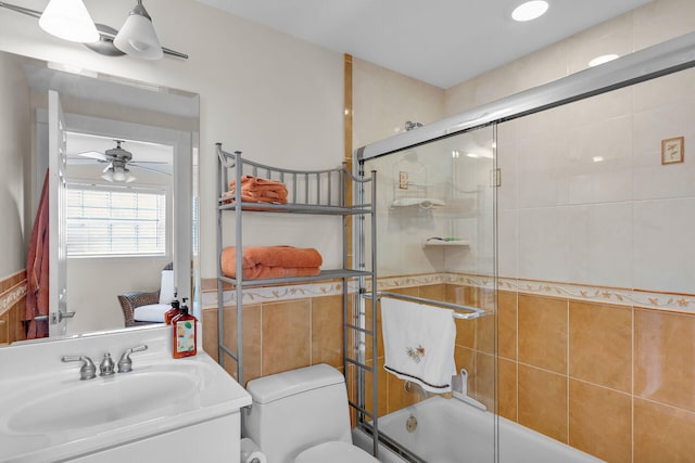 bathroom with tile walls, toilet, a ceiling fan, combined bath / shower with glass door, and vanity