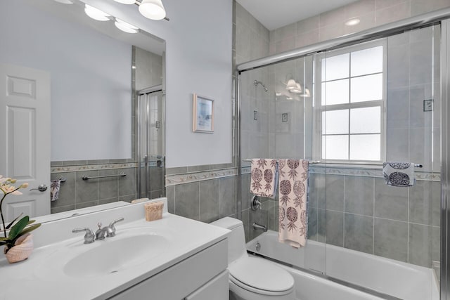 full bathroom with a wainscoted wall, shower / bath combination with glass door, tile walls, toilet, and vanity