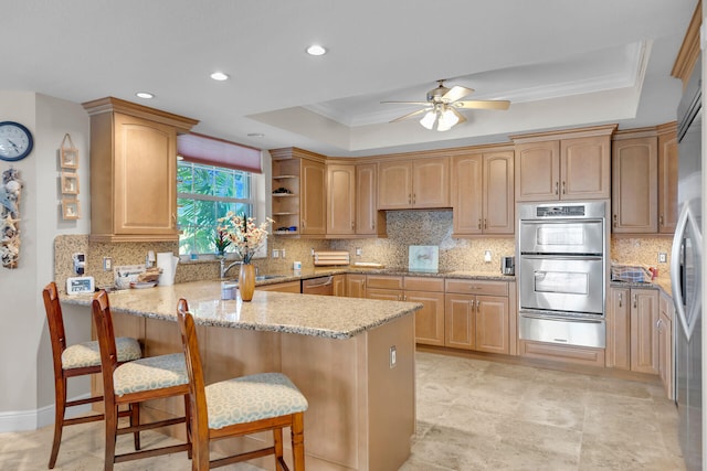 kitchen featuring light stone counters, a peninsula, appliances with stainless steel finishes, a warming drawer, and a tray ceiling