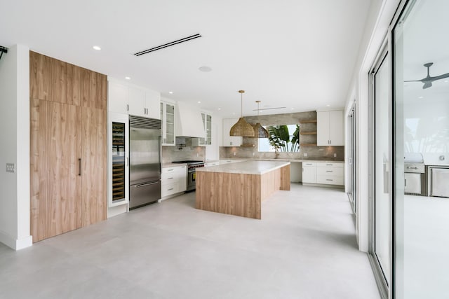 kitchen featuring a center island, hanging light fixtures, premium appliances, decorative backsplash, and white cabinets